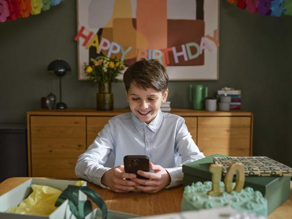 Junge sitzt am Tisch und schaut auf sein Smartphone