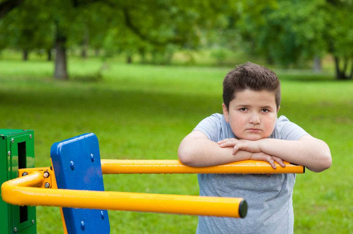 Bildnachweis: © stock.adobe.com / ruslanshug Übergewichtiger Junge lehnt an einem Fitnessgerät im Park