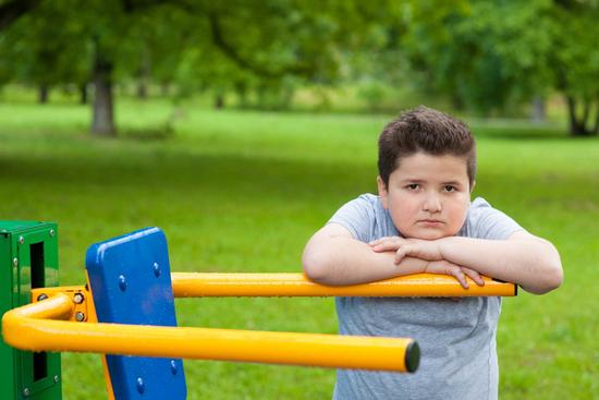 Übergewichtiger Junge lehnt an einem Fitnessgerät im Park