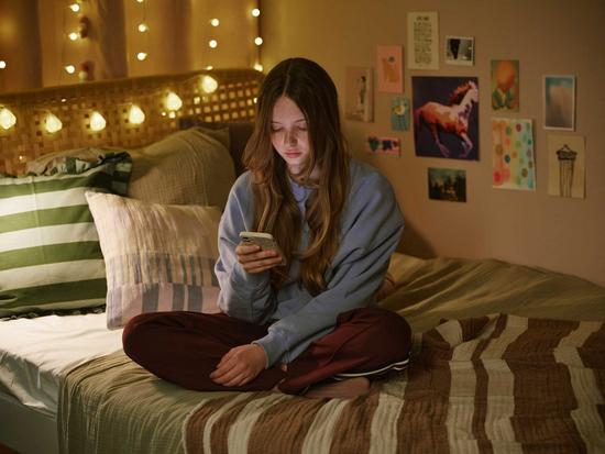 Mädchen sitzt mit ihrem Smartphone auf dem Bett