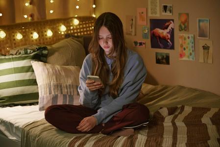 Mädchen sitzt mit ihrem Smartphone auf dem Bett