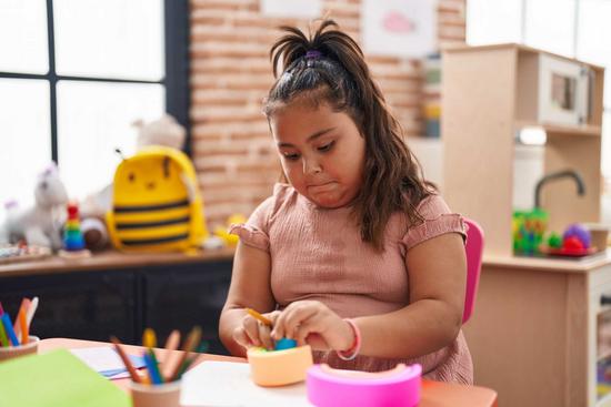 Übergewichtiges Mädchen sitzt im Kindergarten am Tisch und spielt