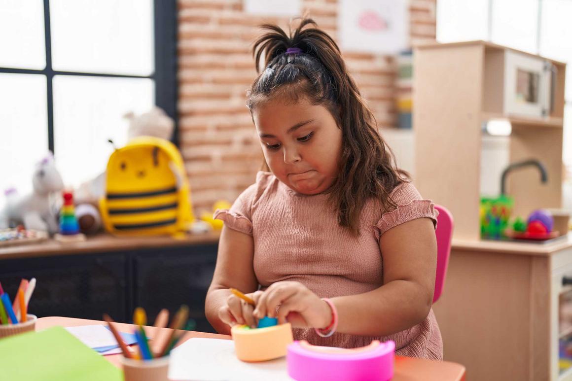 Bildnachweis: © stock.adobe.com / Krakenimages.com Übergewichtiges Mädchen sitzt im Kindergarten am Tisch und spielt