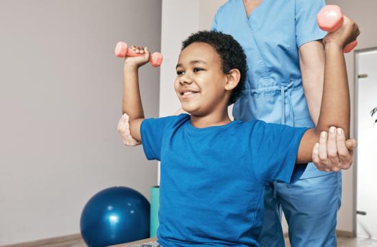 Junge trainiert zusammen mit einer Physiotherapeutin mit Hanteln