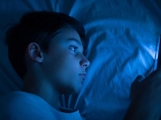 Junge benutzt sein Smartphone im Dunklen im Bett