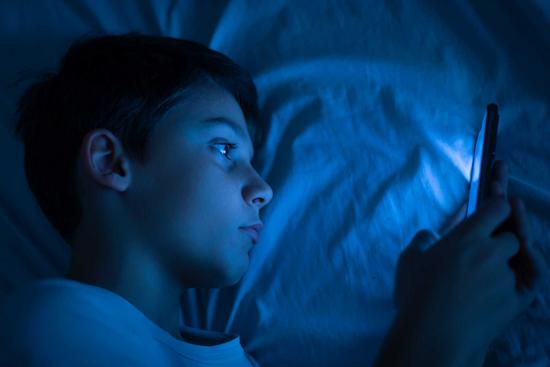 Junge benutzt sein Smartphone im Dunklen im Bett
