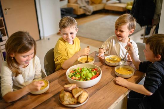 Vier Kinder sitzen am Esstisch und essen Suppe