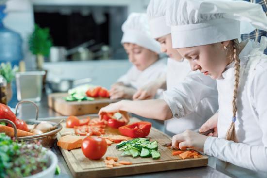 Kinder mit Kochmützen schneiden Gemüse