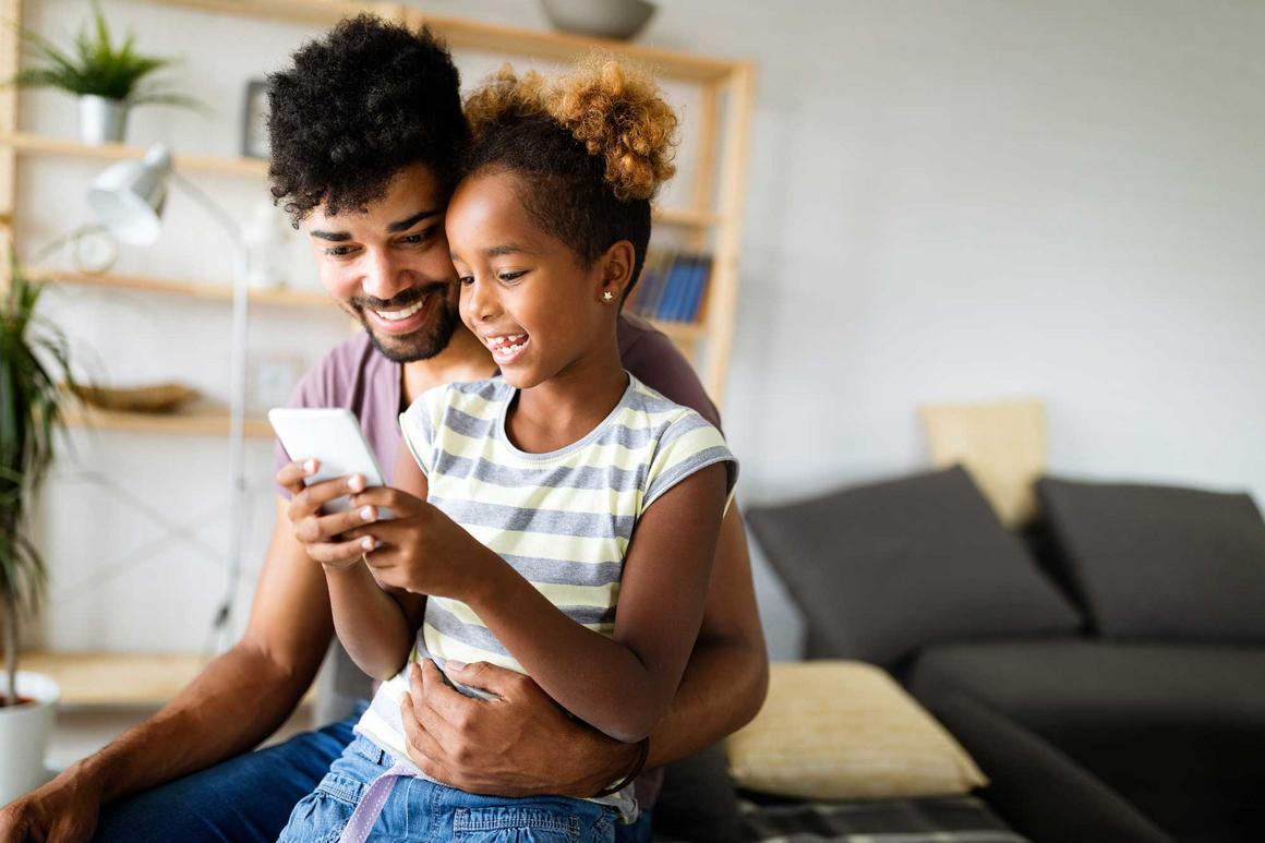 Vater und Tochter sehen sich gemeinsam etwas auf dem Smartphone an und haben viel Spaß dabei