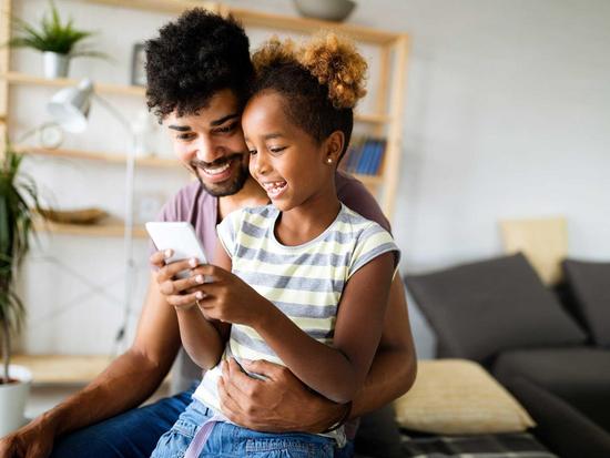 Vater und Tochter sehen sich gemeinsam etwas auf dem Smartphone an und haben viel Spaß dabei
