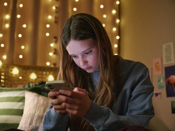 Mädchen sitzt mit ihrem Smartsphone auf dem Bett