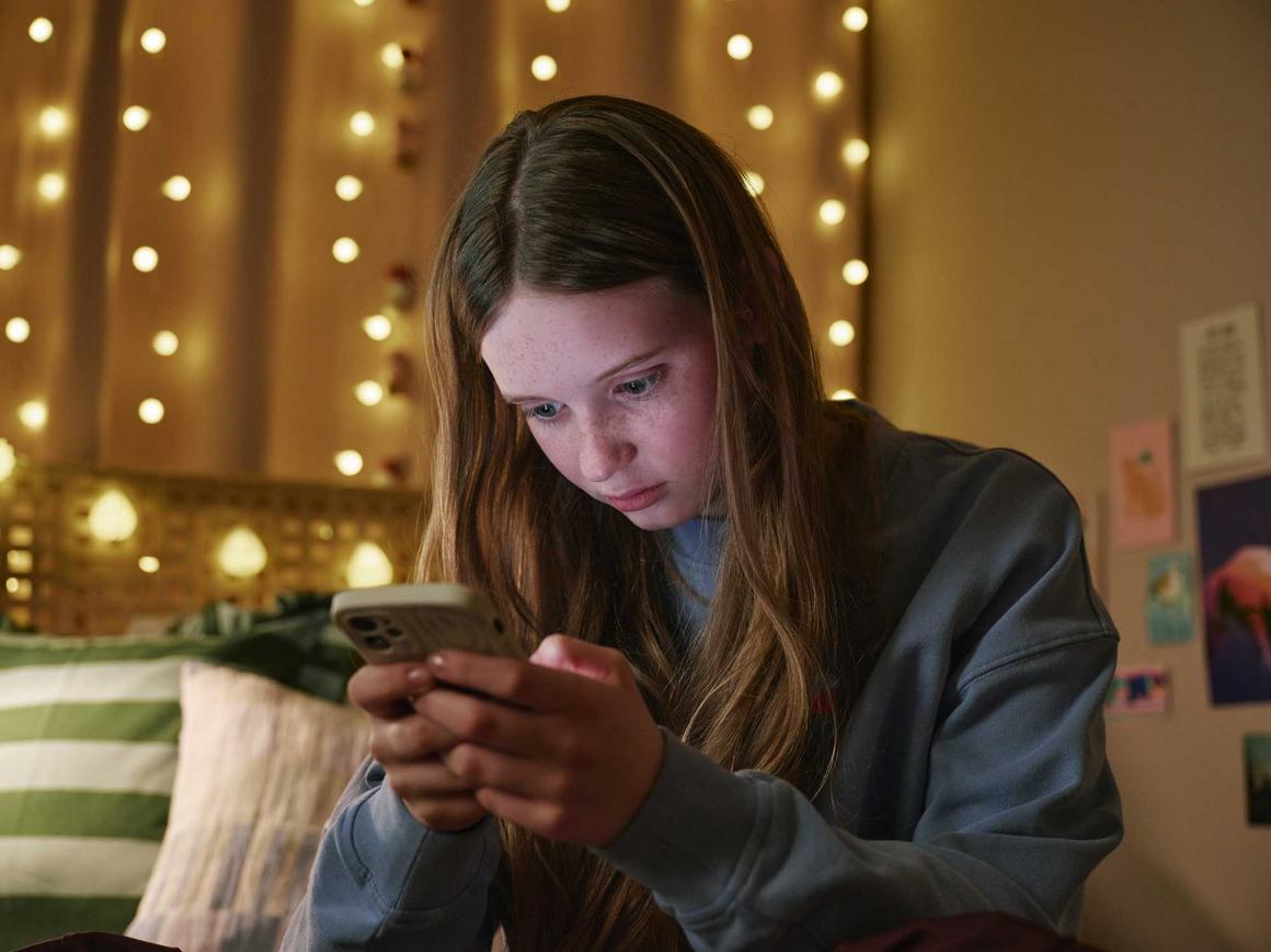 Mädchen sitzt mit ihrem Smartsphone auf dem Bett